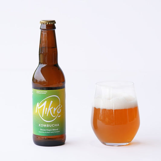 Mikro three hops blend kombucha bottle with gree, yellow label and amber drink in glass with a white background