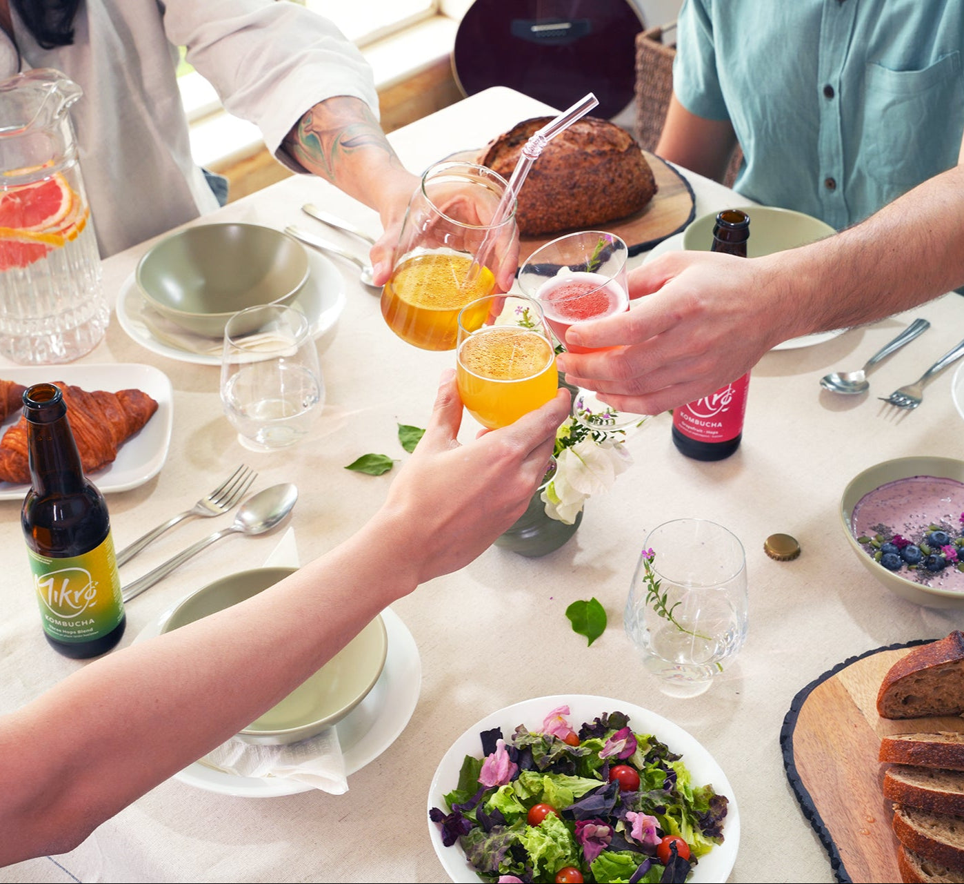 People toasting with Mikro kombucha poured in glasses at a table with food and Mikro kombucha bottles.