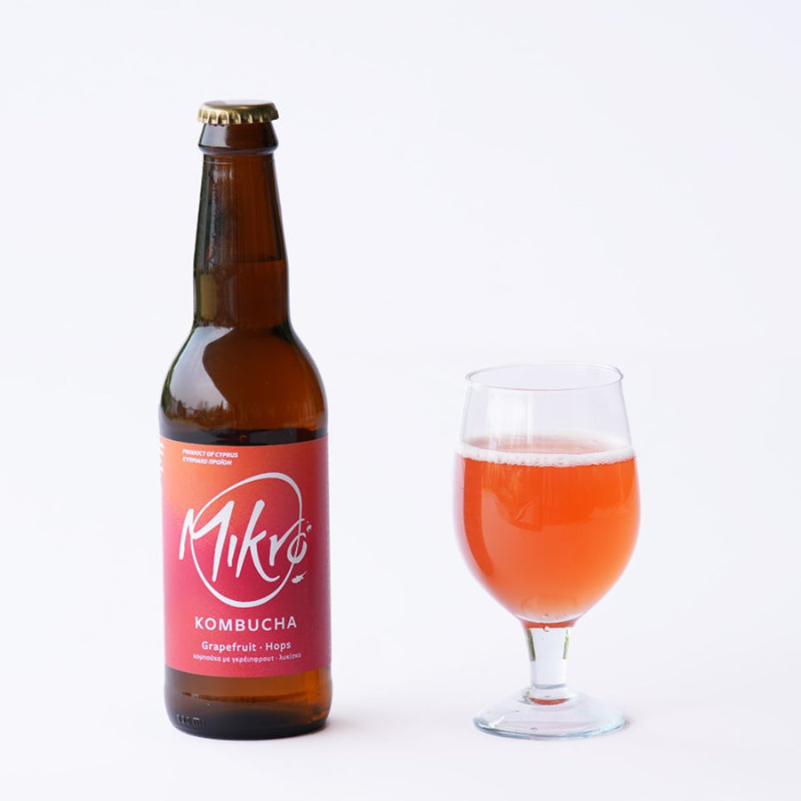 Mikro Grapefruit Hops kombucha bottle with orange, red label and glass of mild orange drink on a white background
