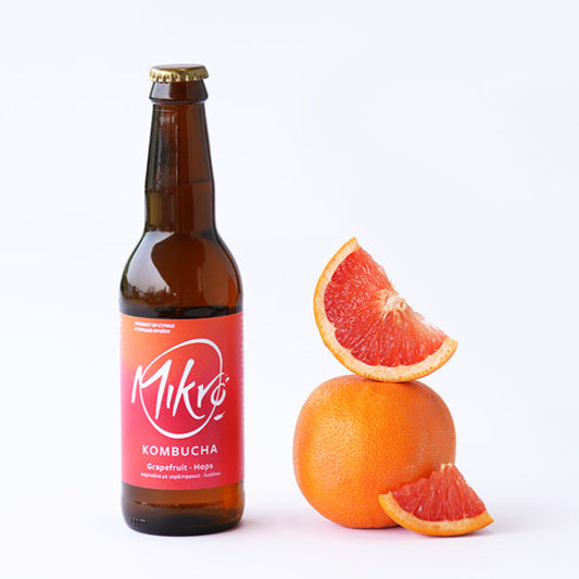 Mikro Grapefruit Hops Kombucha bottle with red and orange label next to grapefruit wedges on a white background