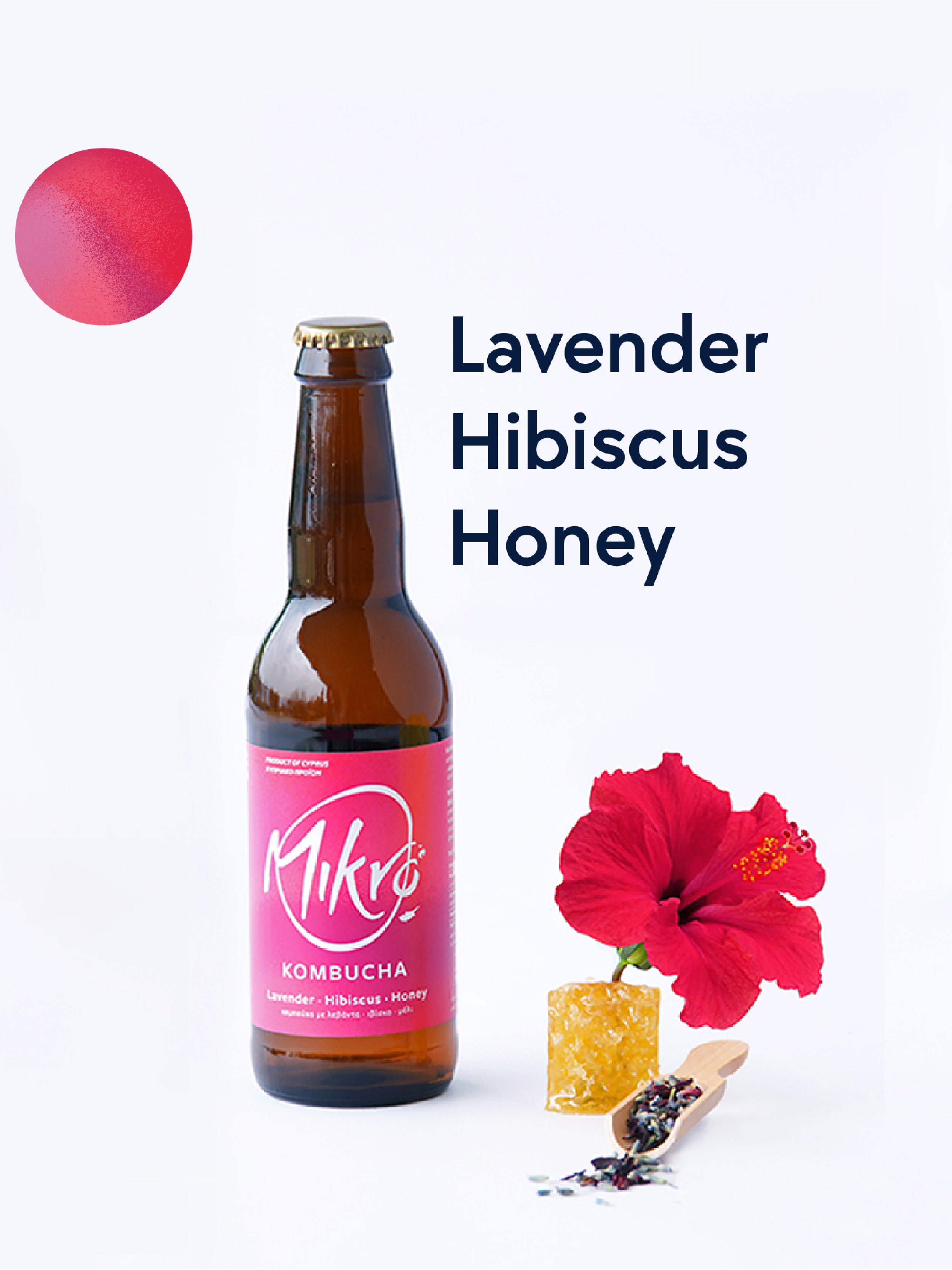 Mikro Lavender Hibiscus Honey Kombucha bottle with bright pink and purple label next to lavender buds, hibiscus flower and honey comb piece on a white background