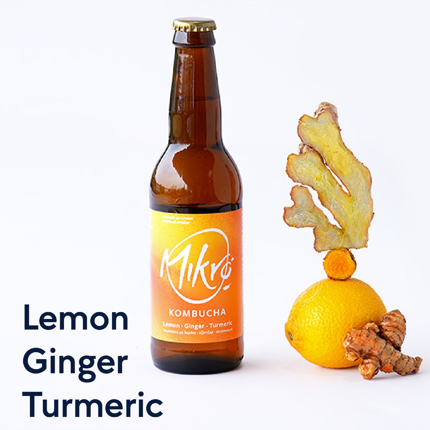 Mikro Lemon Ginger Turmeric kombucha bottle with bright yellow label next to a lemon, ginger, and turmeric pieces on a white background.