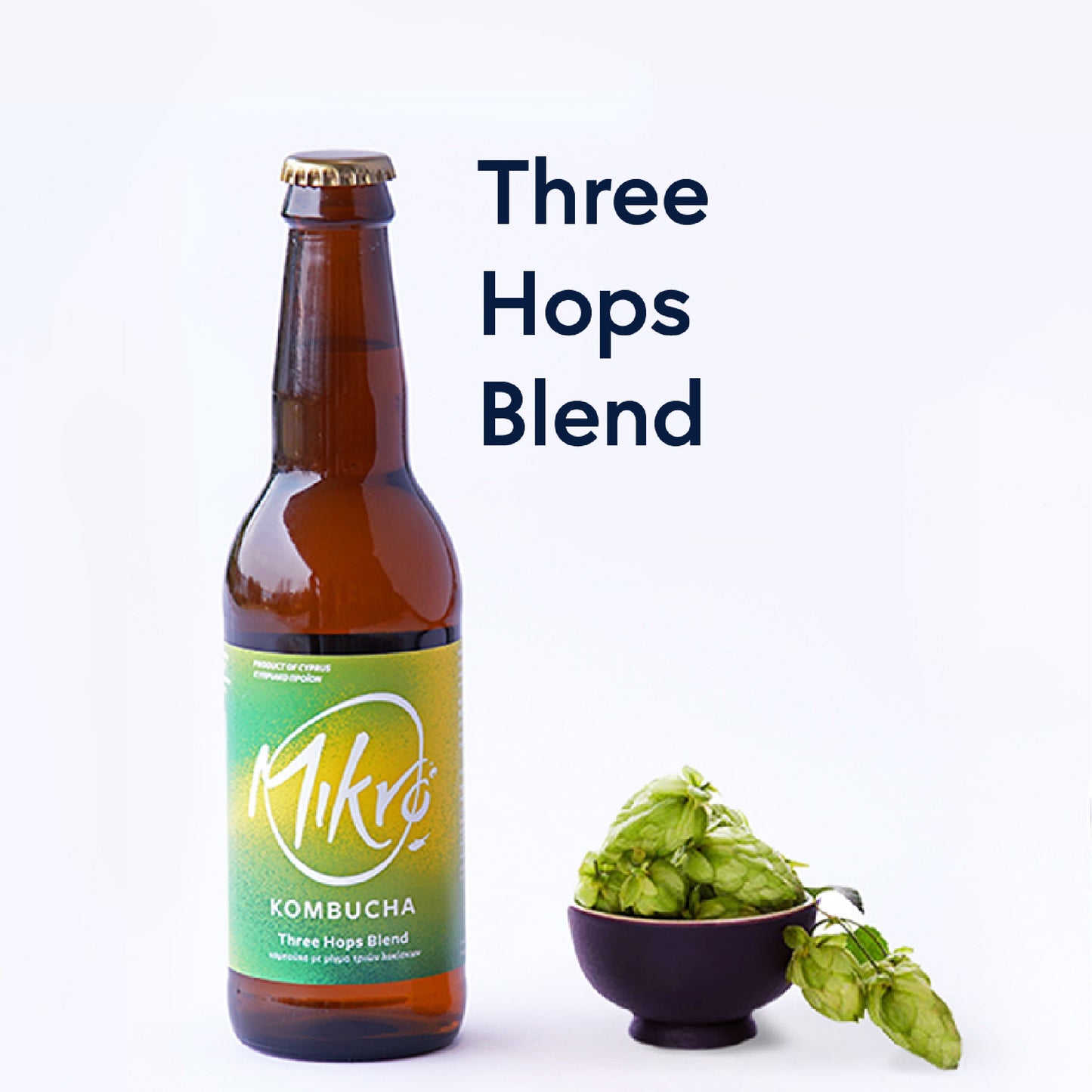Mikro Three Hops bled kombucha bottle with bgright green and yellow label next to a bowl of hops buds on a white background