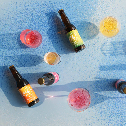 Mikro kombucha bottles and glasses with colourful sparkling drinks on a blue surface.