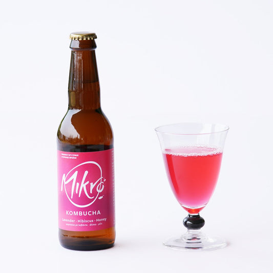 Mikro lavender hibiscus kombucha bottle with pink purple label and glass of pink drink on a white background