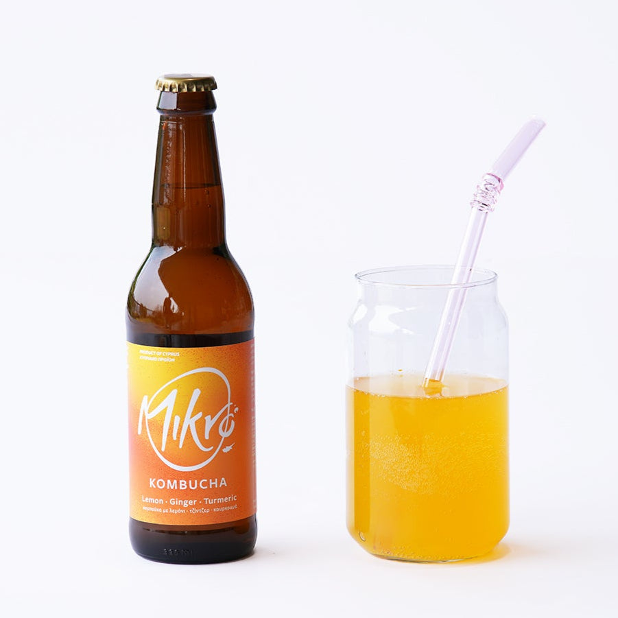 Mikro lemon ginger turmeric kombucha bottle with yellow, orange label and glass with yellow drink and straw on a white background
